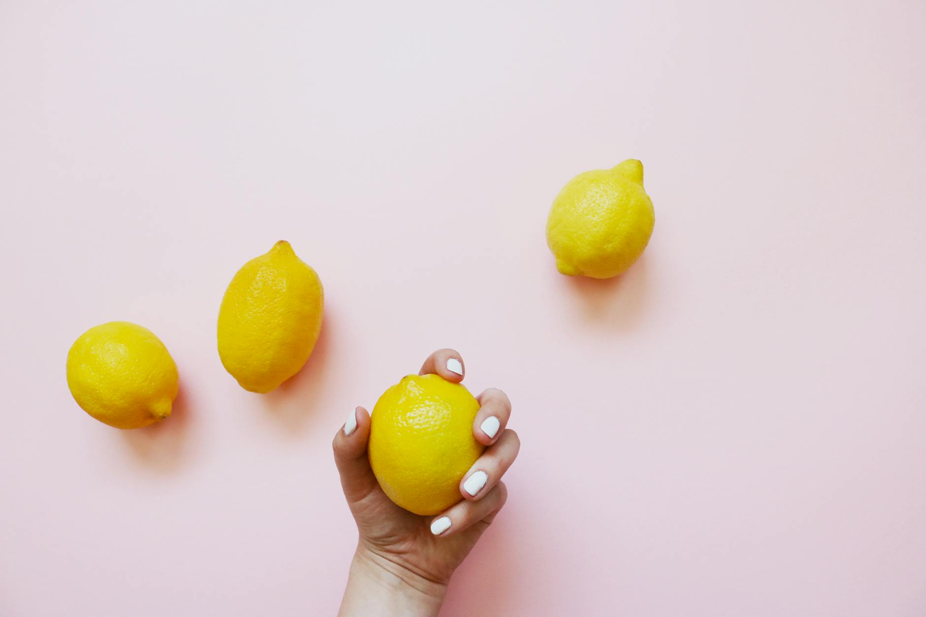 A hand holding a fresh lemon on a soft pink background, symbolizing refreshing intimacy