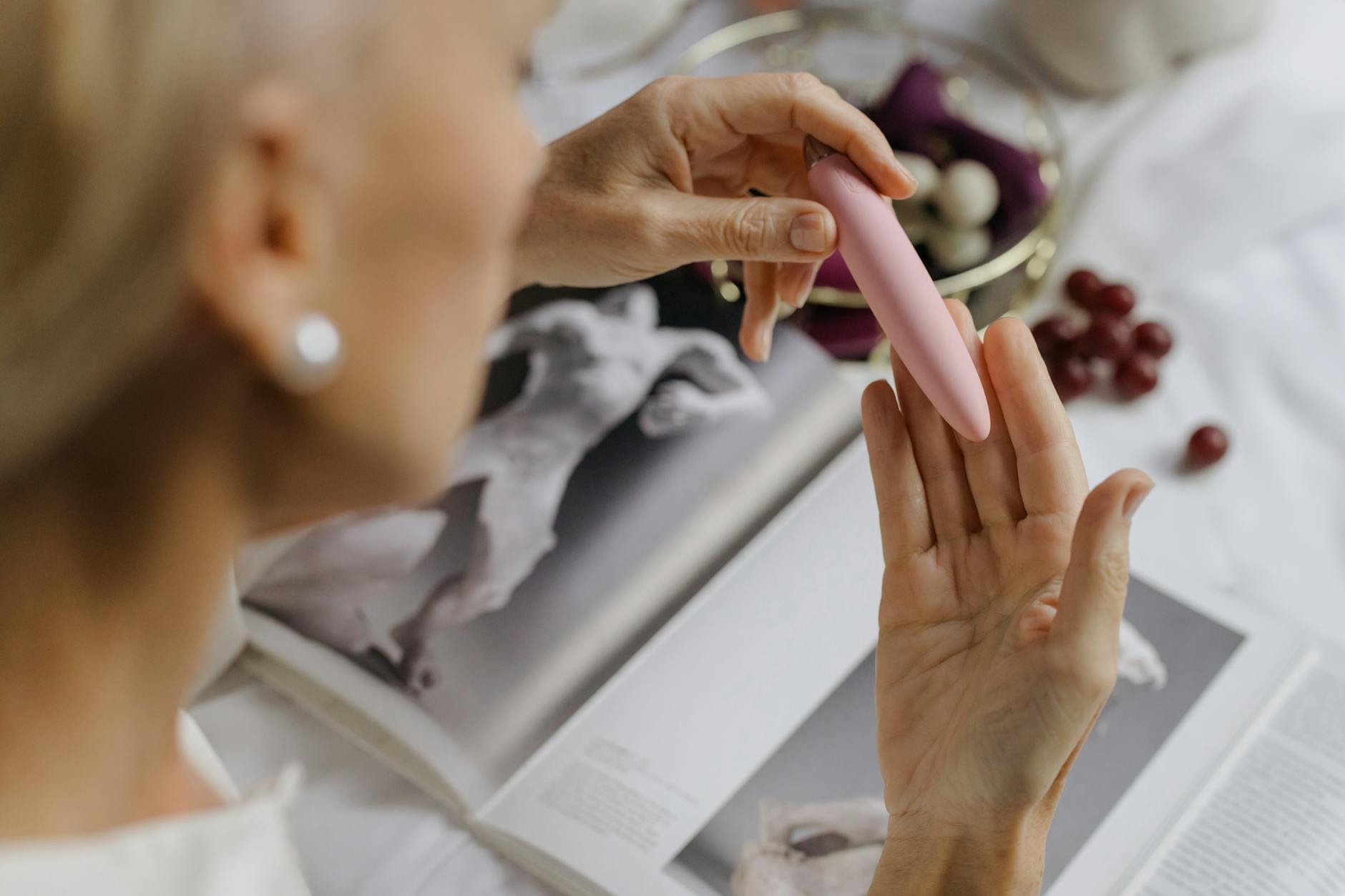 A close-up of a woman holding a vibrator with art and personal items in the background, representing intimate self-care during emotional healing.