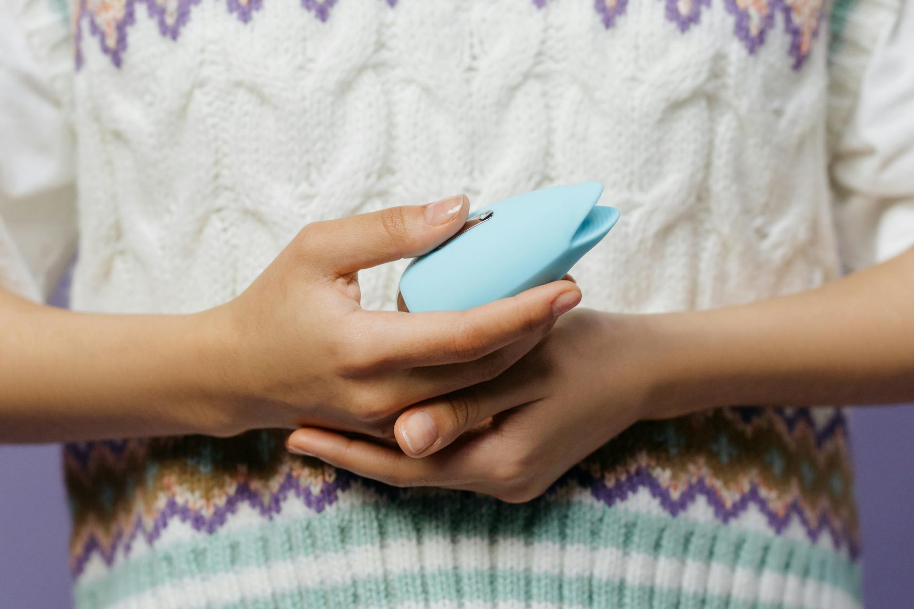 A lemon clitoral vibrator held gently in hand against a purple background, representing self-love and personal pleasure.